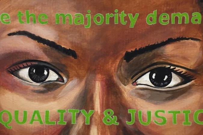 Painting of a woman’s eyes. Painted over her forehead and cheeks are the words “we the majority demand/EQUALITY & JUSTICE” 