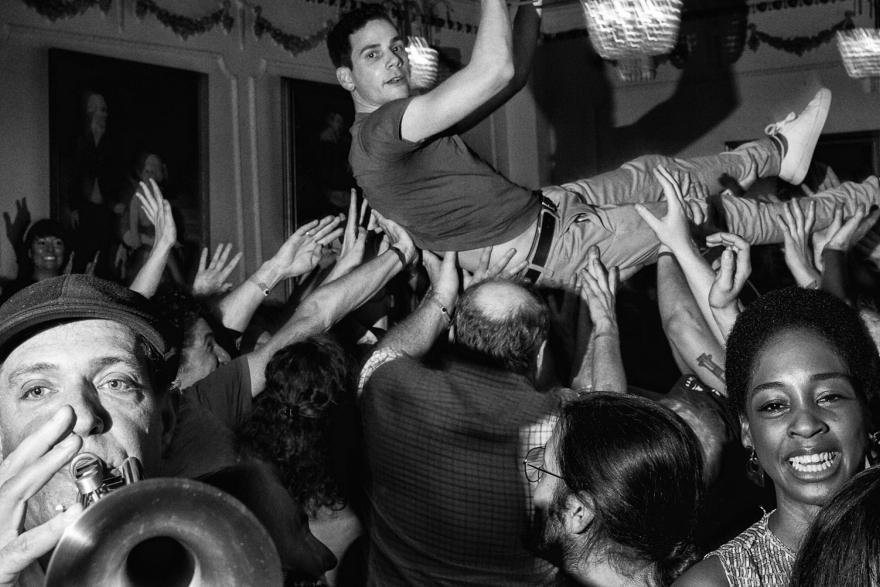 A crowd of people, including two people playing instruments in the foreground and a man crowdsurfing in the background