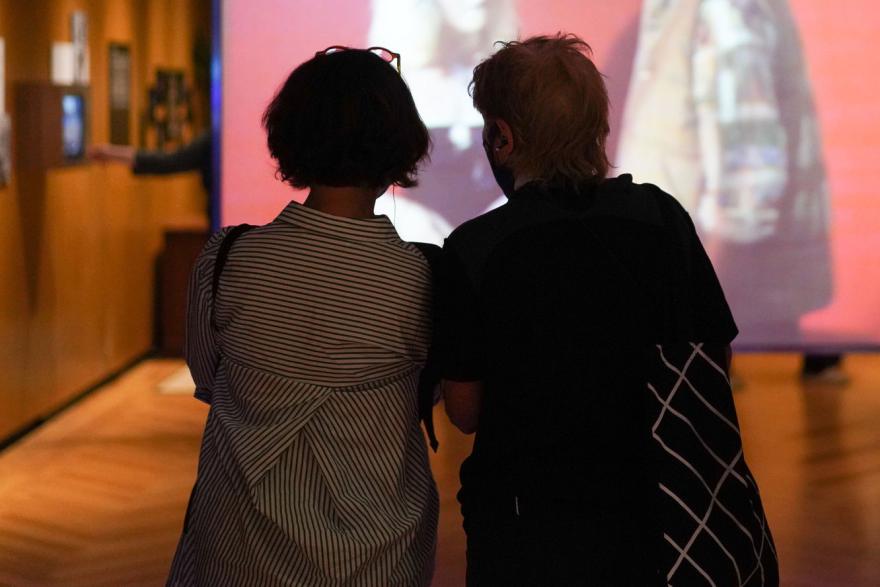 Two women stand in front of an illuminated screen in a gallery.