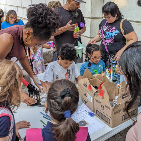 A group of young people stand around a table making crafts with instructors.