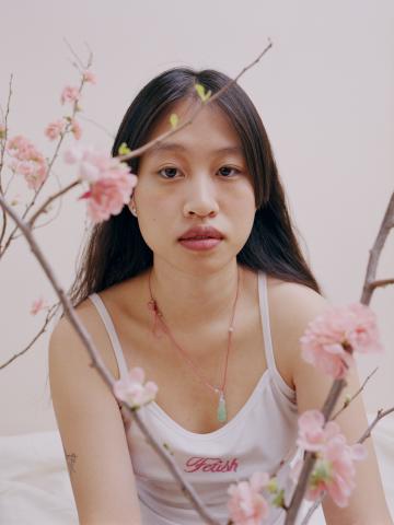 A woman poses behind two cherry blossom branches. 