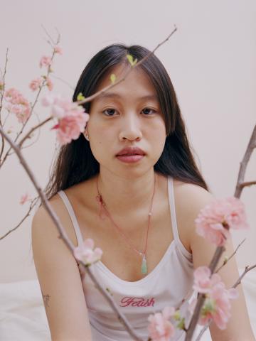 Une femme pose derrière deux branches de fleurs de cerisier.