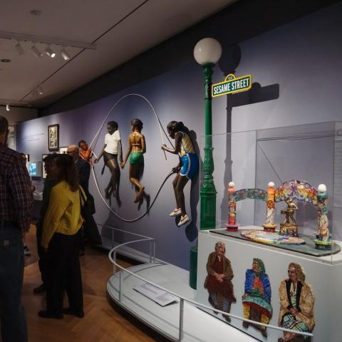 Vista da instalação da exposição "This Is New York" apresentando a escultura Double Dutch de Rigobertto Tores e John Aherns, a placa de rua original da Vila Sésamo e uma macquete de mosaico de Manny Vega.