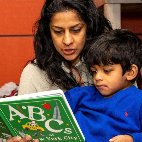 Une mère tient son fils sur ses genoux pendant qu'elle lui lit un extrait du livre "ABC's of New York City".