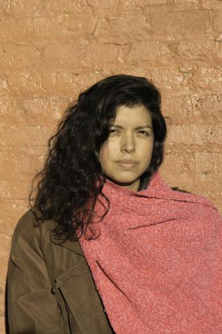 A woman wearing a scarf stands in front of a brick wall.