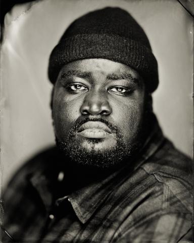 A man in a wool hat looks into the camera lens. 