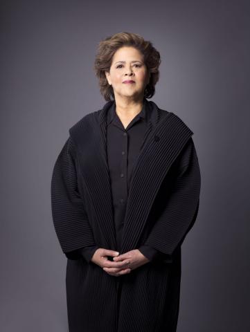 Anna Deavere Smith vestindo preto fica contra um pano de fundo cinza