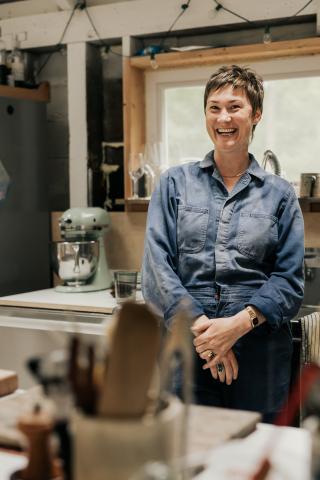 A woman in a denim shirt smiles in a kitchen. 