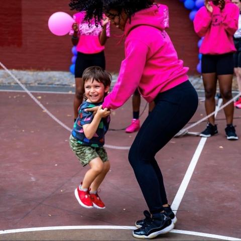 A young boy jumps rope while holding onto the instructors hands.