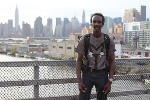 Kurt Boone, New York Responds Juror, stands on a bridge or overpass with the NYC skyline behind him