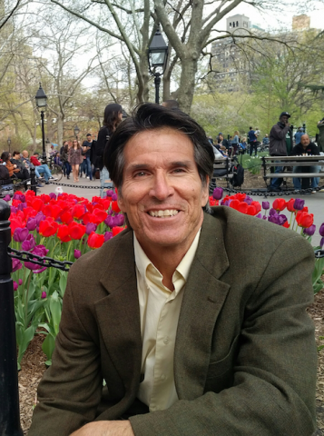 Photograph of Rick Chavolla in a public park seated or kneeling in front of a group of red and purple tulips