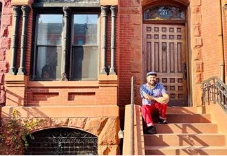 A man sits on the steps of a brownstone building