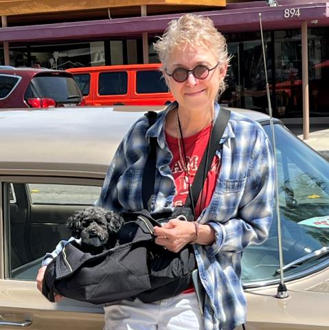 A woman poses with a small dog in a bag. 