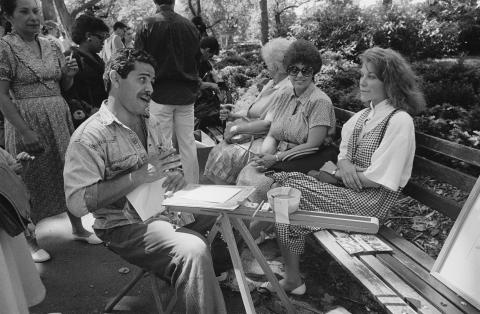 A man talks to two women as he draws their portraits.