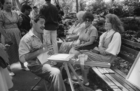 A man talks to two women as he draws their portraits. 