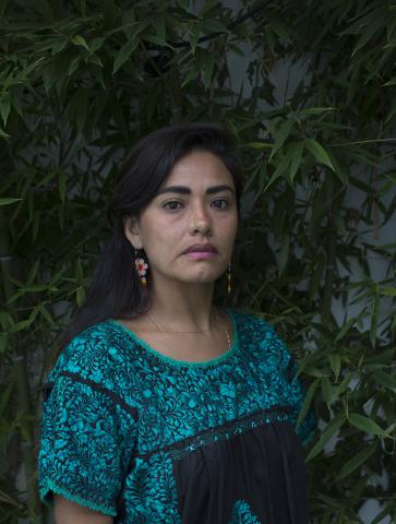 A woman stands in front of a plant wall. 