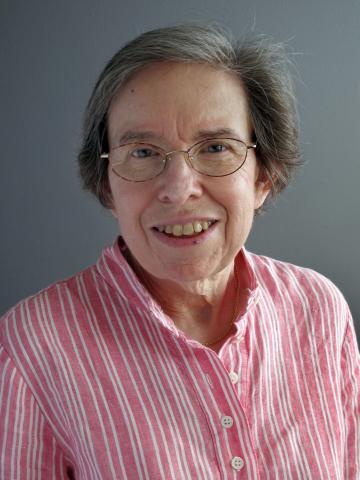 A woman in glasses and a pink shirt smiles at the camera. 