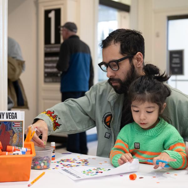 A man in glasses and a small child make art at a table. 