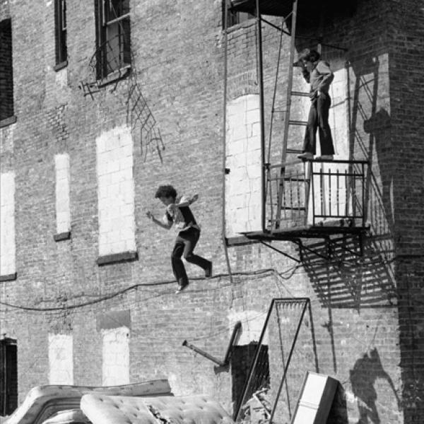 A street play photograph by Martha Cooper of a boy jumping from fire escape at the Lower East Side.