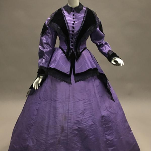 Un vestido 1866 de moiré de seda púrpura con terciopelo negro y adornos de encaje negro que se pueden usar tanto de día como de tarde.