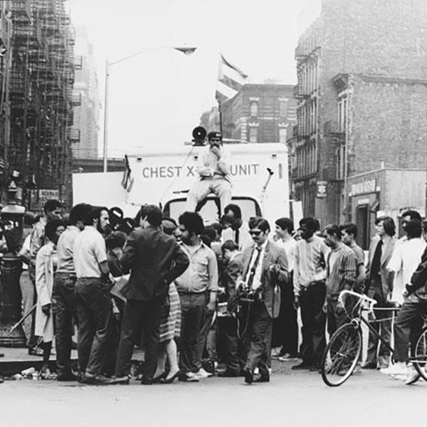 A group of young activists and journalists stand in front of a mobile x-ray truck, which is flying a Puerto Rican flag. 