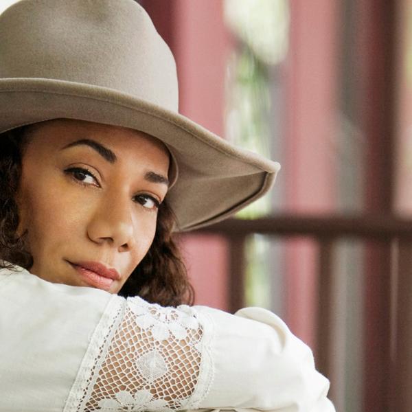 Un portrait en gros plan de Martha Redbone. Elle porte une robe blanche à manches longues et un chapeau bordé de beige grisâtre.