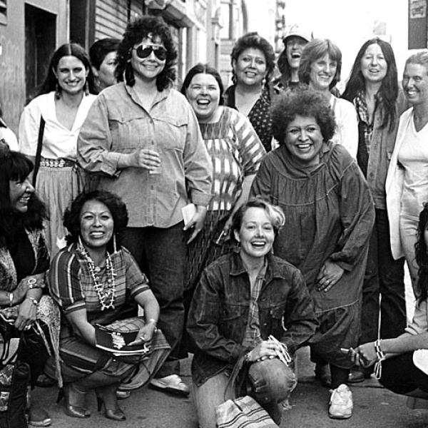 Photograph of artists from the exhibition, Women of Sweetgrass, Cedar and Sage, friends and community members outside the American Indian Community House Gallery taken in 1985. 