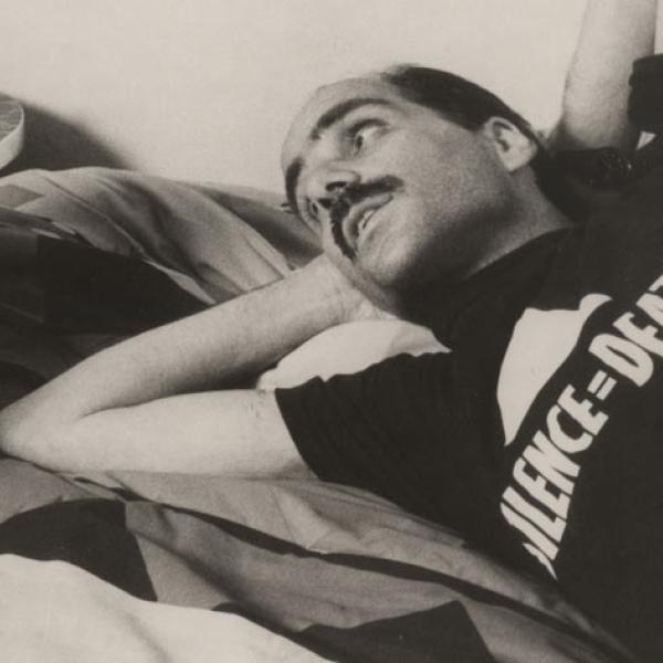 Close-up of a male AIDS patient wearing an ACT UP t-shirt and lying on a bed