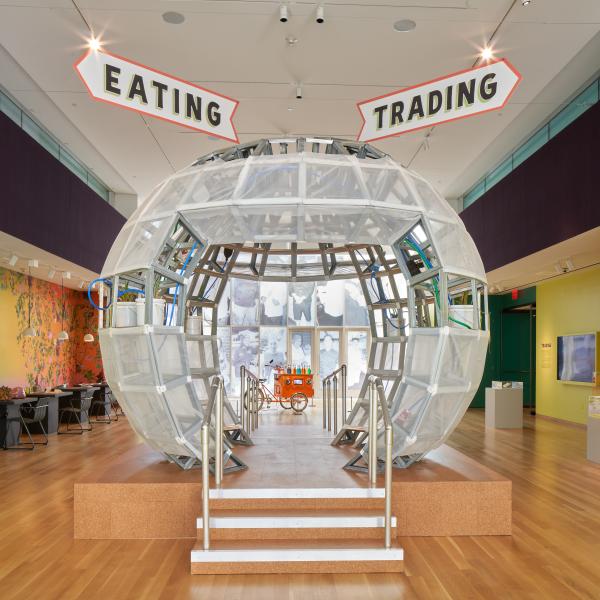 A large clear sphere, similar to a snowglobe sits at the center of the image with signs that read 'eating' and 'trading' above it. 