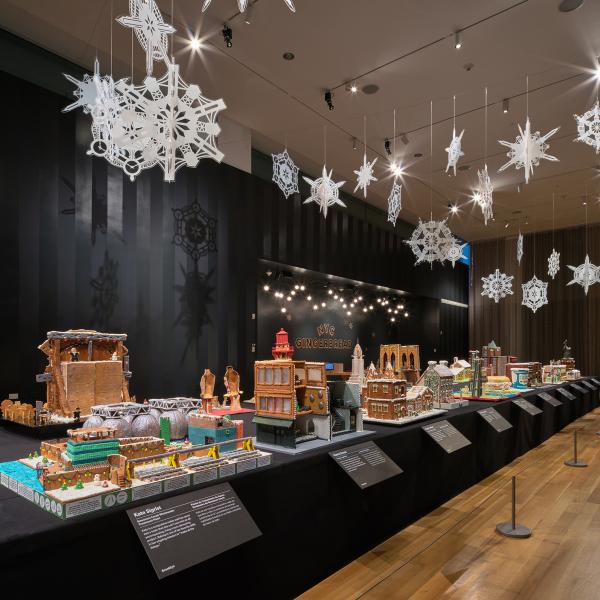 A long table with gingerbread houses inspired by New York, with lights and snowflakes hanging above