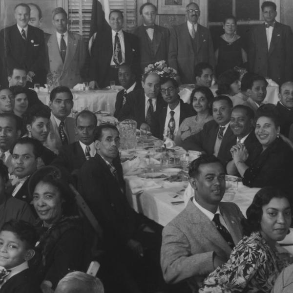 Imagem em preto e branco de um grupo sentado ao redor de uma grande mesa