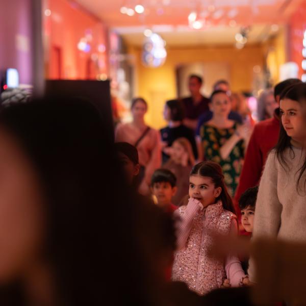 An image focused on a little girl looking mesmerized in a crowd of people walking down a colorful hallway