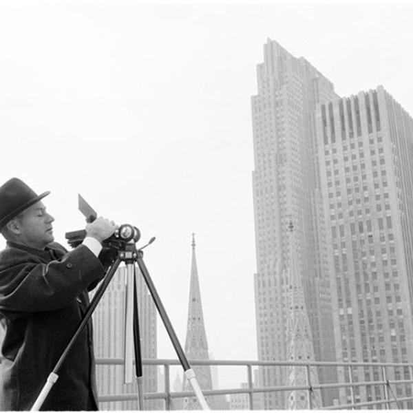 Man adjusting his camera on a tripod with the New York City skyline in the background.