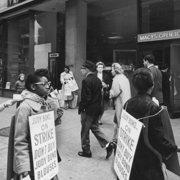 A group of on-strike workers march outside Macy’s while wearing signs encouraging people to not buy Judy Bond blouses 