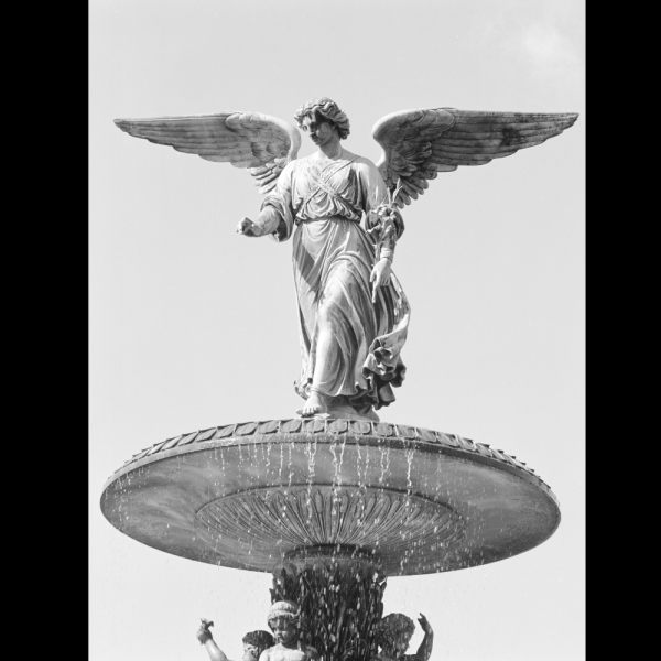 Bethesda Fountain: A black-and-white photograph shows a winged angel statue standing atop a large fountain, arms gently extended as water cascades below against a bright, open sky.