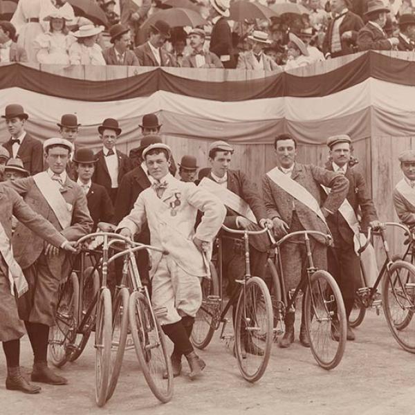 Os homens se alinham com suas bicicletas enquanto os espectadores observam de assentos elevados antes do The Evening Telegram Bicycle Parade