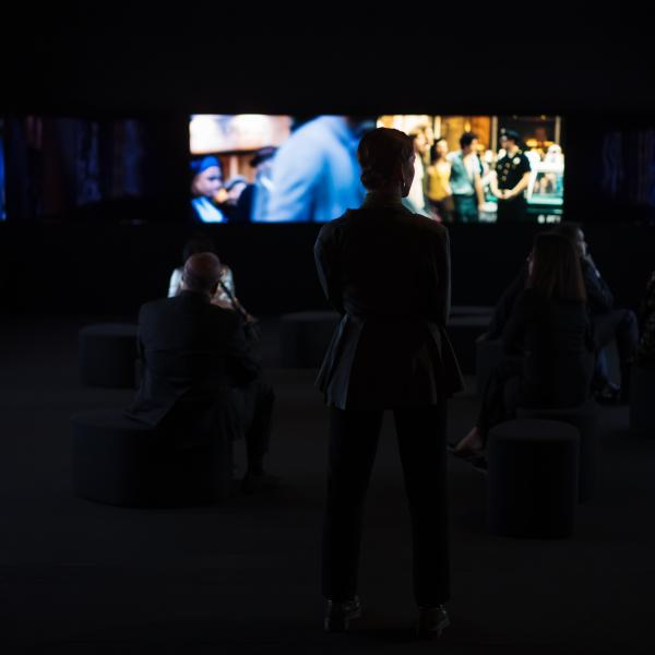 La silueta de una mujer parada frente a varias pantallas que muestran imágenes borrosas de películas.