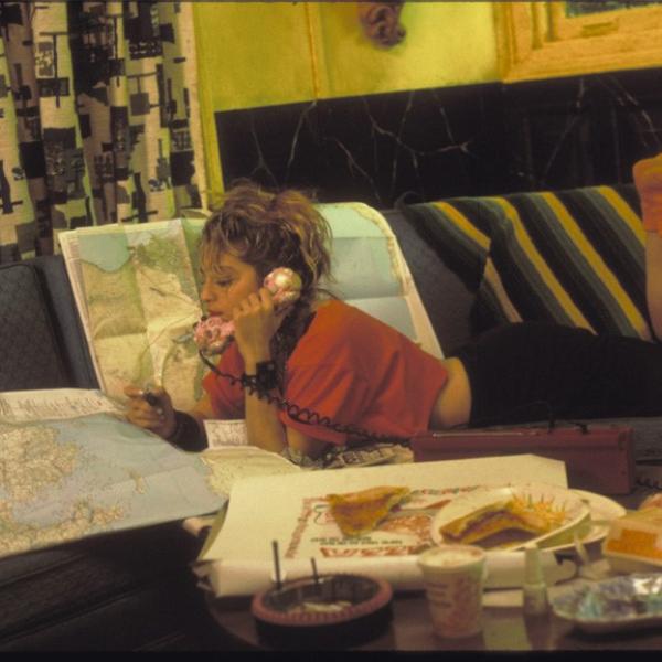 《拼命寻找苏珊》剧照。 麦当娜趴在沙发上看地图，手里拿着一部粉红色的电话。