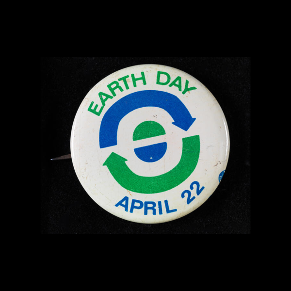 Un bouton blanc indiquant le Jour de la Terre le 22 avril avec des flèches bleues et vertes et des demi-cercles qui symbolisent le recyclage et la terre