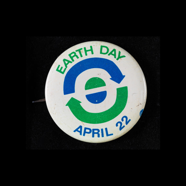 A white button that reads Earth Day April 22 with blue and green arrows and semi circles that symbolize recycling and the earth