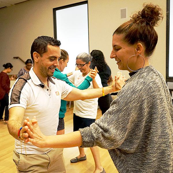 Educators, holding hands in pairs, taking part in a salsa dance lesson during the course.