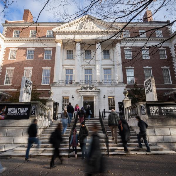 A crowd of visitors walks up the front steps toward the Museum's building