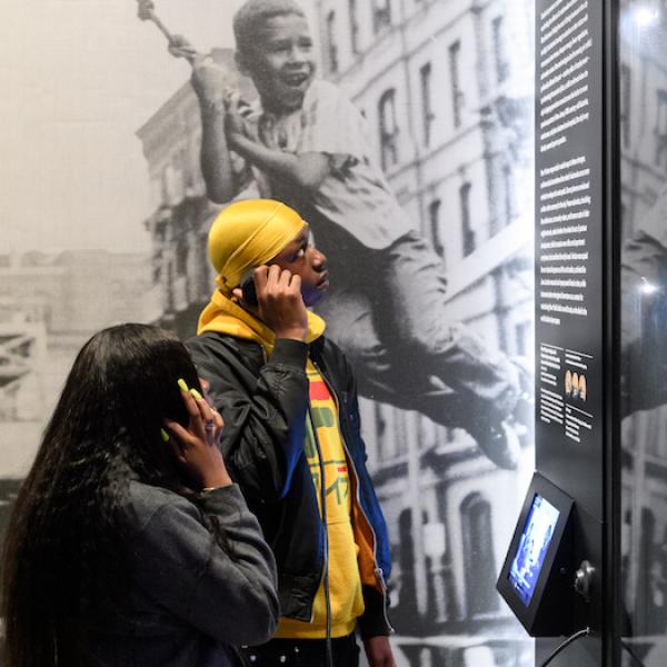 Dos estudiantes usan audífonos para escuchar una grabación en la galería "World City", parte de "New York at Its Core".