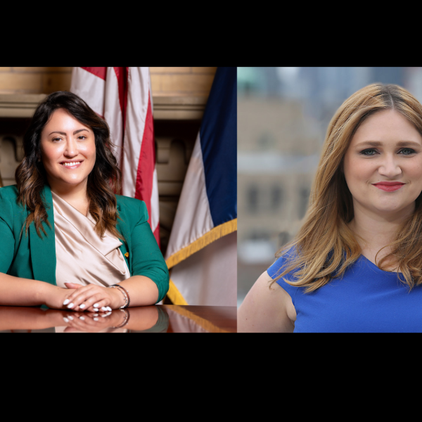 Two women in separate portraits: the woman on the left is seated at a desk with U.S. flags in the background, wearing a green blazer and light blouse; the woman on the right is standing outdoors with a cityscape backdrop, wearing a royal blue dress and smiling