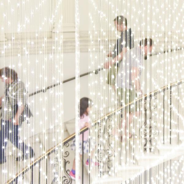 A crowd ascends a spiral staircase behind a light installation