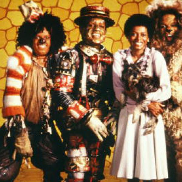 Four people in costumes stand in front of a yellow brick backdrop. 