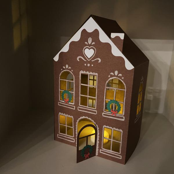 The image shows a lighted model of a dark brown building decorated with white trimming and two wreaths