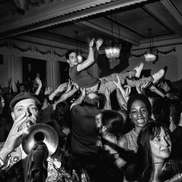 A crowd of people, including two people playing instruments in the foreground and a man crowdsurfing in the background
