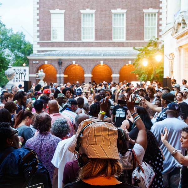 L'arrière de la tête de DJ Misbehaviour est visible devant une mer de danseurs sur la terrasse avant du Musée.