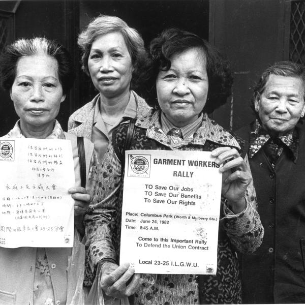 Members of the labor union ILGWU Local 23-25 look directly into the camera and hold up English and Chinese-language flyers in support of the strike against garment factories in New York City’s Chinatown. 